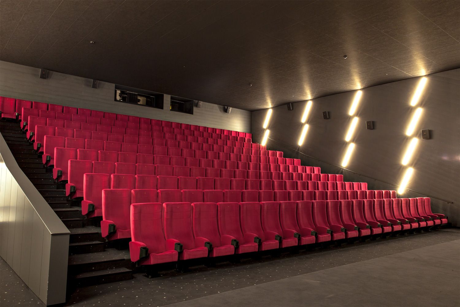 Rising rows of turquoise upholstered seats, with the white balustrade of the stairs on the left.