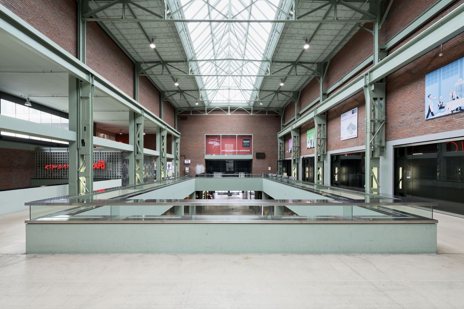 A two-storey foyer with brick walls, green-painted steel columns and a glass roof, galleries all around and the cinema's neon
