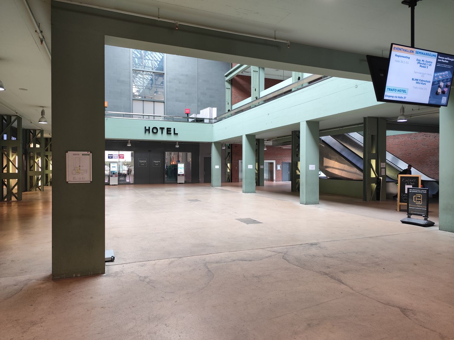 An open concourse with green columns, the word Hotel above the entrance, an escalator and a display board listing the day's e